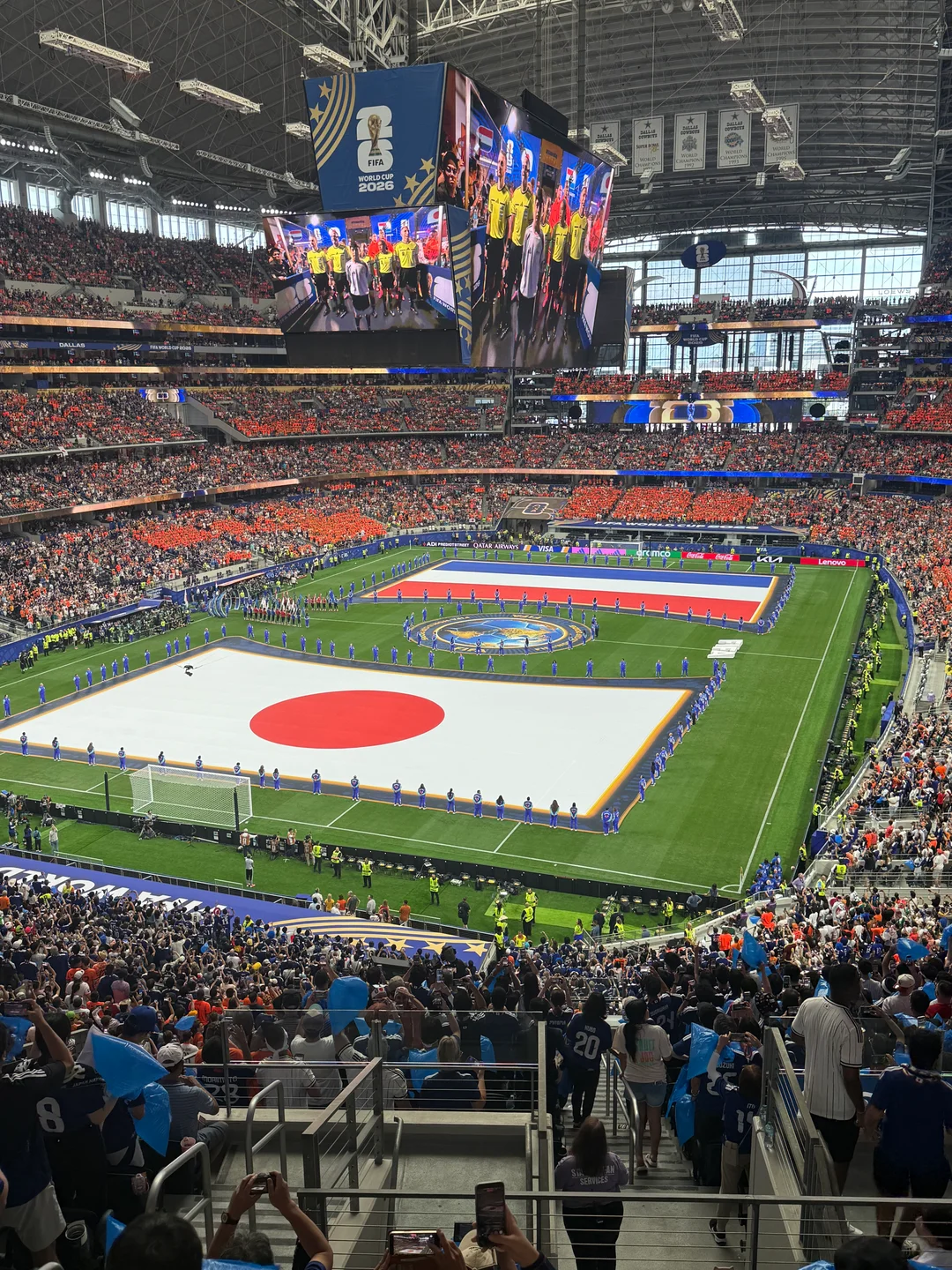 A football stadium filled with spectators, with Japanese and Dutch flags spread across the pitch.