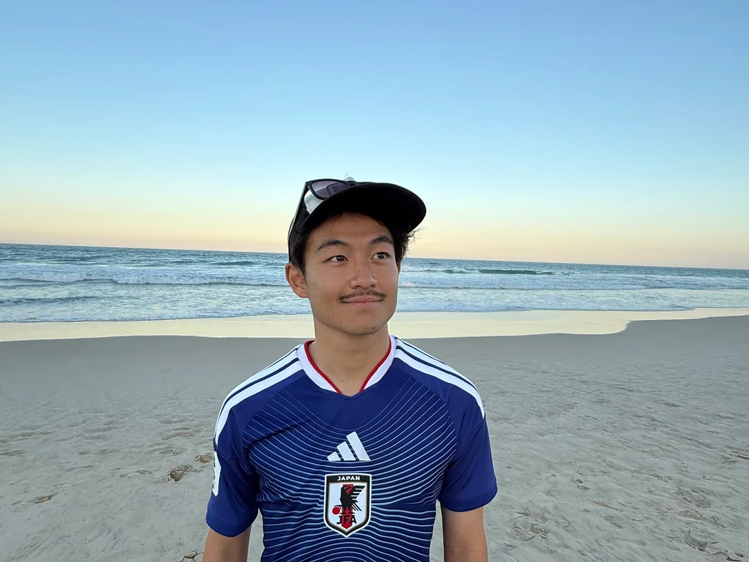 Shinya wearing a Japan football shirt on a beach, with the sea behind him.